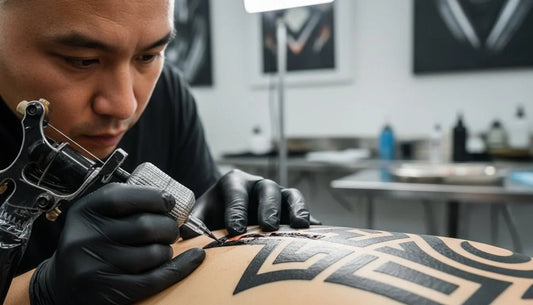 A tattoo artist tattoos a deep-black ornamental design onto the client's back.